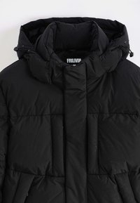 Veste rembourrée noire avec un col haut, texture matelassée visible, cordon de resserrage sur la capuche et patte de boutonnage avant sans matériel visible.