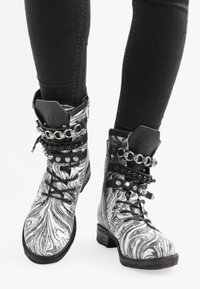 Botas de tobillo en blanco y negro con efecto mármol, adornadas con remaches de metal y cadenas, que cuentan con cordones y un tacón resistente para mayor tracción y soporte.
