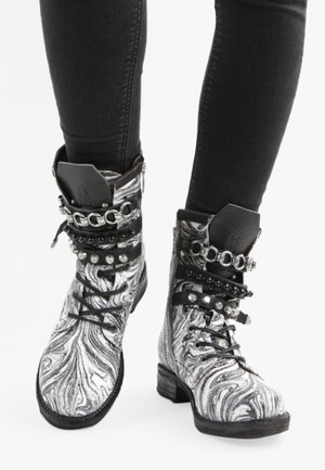 Schwarz-weiße marmorierte Ankle Boots mit Metallnieten und Ketten, die Schnürsenkel und einen stabilen Absatz für Halt und Unterstützung bieten.