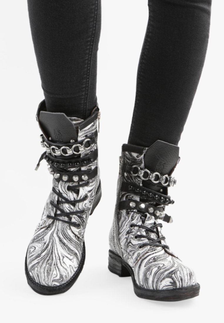 Botas de tobillo en blanco y negro con efecto mármol, adornadas con remaches de metal y cadenas, que cuentan con cordones y un tacón resistente para mayor tracción y soporte.