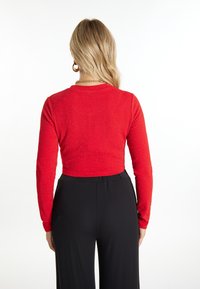 Top rosso a maniche lunghe, cropped, con finitura testurizzata e glitterata abbinato a pantaloni neri a vita alta. Mostra la vista posteriore con scollatura rotonda.