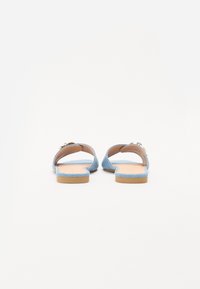 Blå platta slidesandaler med mjuk mocka textur, öppen baksida och minimalistisk design. Har en liten guldaccent nära remmen.