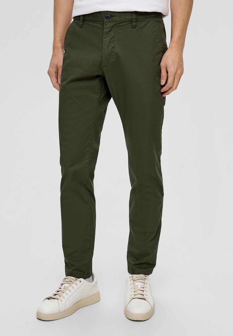 Zielone oliwkowe spodnie bawełniane o slim fit, z bocznymi kieszeniami i zapięciem na guziki z przodu, w zestawieniu z białymi sneakersami.