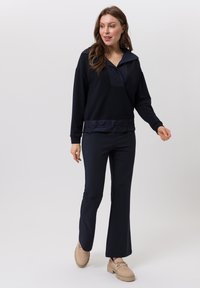 Donkerblauw sporttop met een kraag en een gemêleerd paneel. Gecombineerd met slim-fit navy broek en beige instappers.