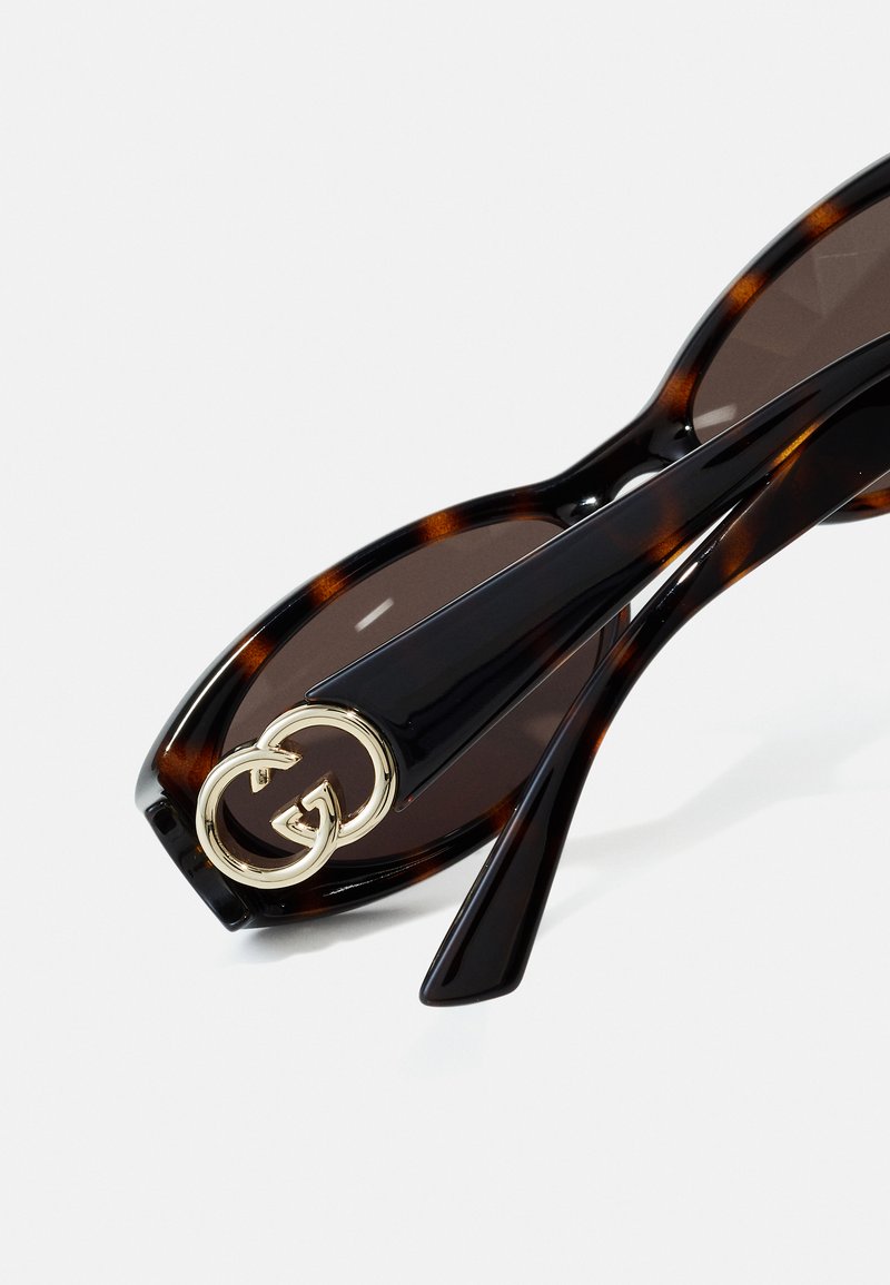 Tortoiseshell sunglasses with dark lenses; black frames feature a gold GG logo accent on the temple. Smooth, glossy texture throughout.