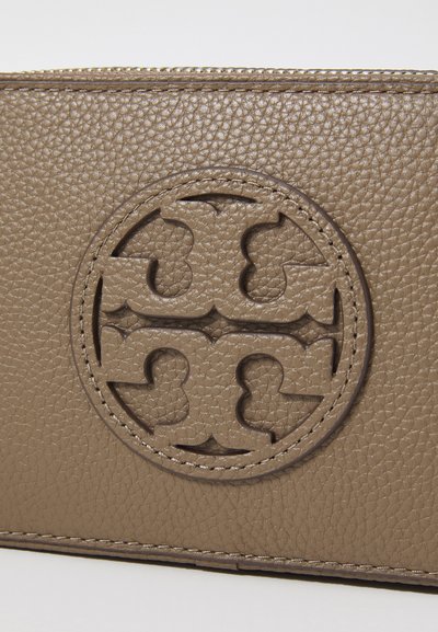 Portefeuille en cuir texturé marron avec un design de logo en forme de découpure circulaire, bordé d'une finition lisse et doté de détails de couture visibles.