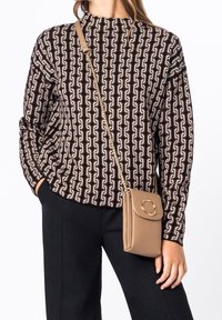 Brun og creme mønstrede sweater med høj hals; parret med en tan crossover taske med cirkulært element og guld kædeder.