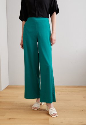 Teal vide benbukser laget av et lett stoff, med en flat frontliv. Brukt med hvite blokkhæl sandaler.