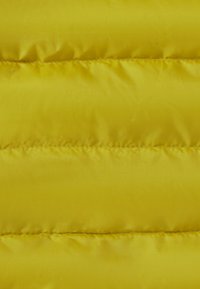 Tessuto giallo trapuntato con cuciture orizzontali, che mostra sezioni morbide e imbottite e una superficie liscia e lucida.