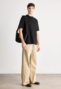 Μαύρο βαμβακερό μπλουζάκι με μικρό λογότυπο, σε συνδυασμό με φαρδιά μπεζ τζιν παντελόνια με εμφανή ραφή και μαύρα παπούτσια. Ρυθμιζόμενη μαύρη τσάντα ώμου.