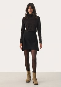 Haut à manches longues noir à rayures avec un col montant, associé à une jupe noire. Le modèle porte des bottes à talons beige en daim avec un détail de boucle.