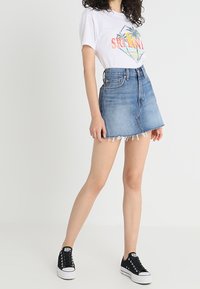 Minifalda de mezclilla con dobladillo deshilachado, lavado azul claro, diseño de cintura alta. Combinada con una camiseta gráfica blanca y zapatillas de lona negras.