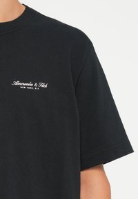 Sort bomulds t-shirt med korte ærmer, der har et hvidt broderet logo på brystet med teksten "Abercrombie & Fitch, New York, N.Y."