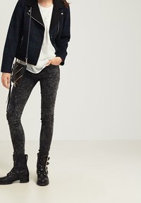 Černý a zelený károvaný blejzr, bílý top, vybledlé černé skinny džíny a černé šněrovací kotníkové boty se zlatými detaily.