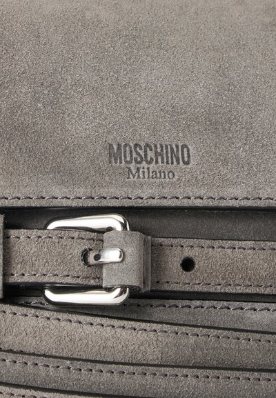 Γκρι σουέτ δερμάτινη επιφάνεια με λογότυπο Moschino Milano και ασημένια αγκράφα σε ρυθμιζόμενο λουράκι.