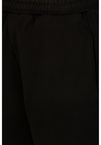 Gros plan sur un pantalon de survêtement en tissu noir montrant la ceinture élastique et la couture de la poche latérale.