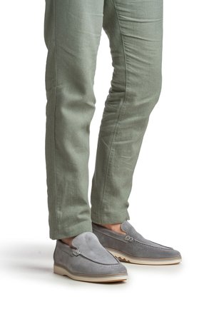 Grau melierte Slipper aus Wildleder mit glattem Obermaterial, kontrastierender weißer Sohle und dezenten Nähten, kombiniert mit hellgrünen, strukturierten Hosen.