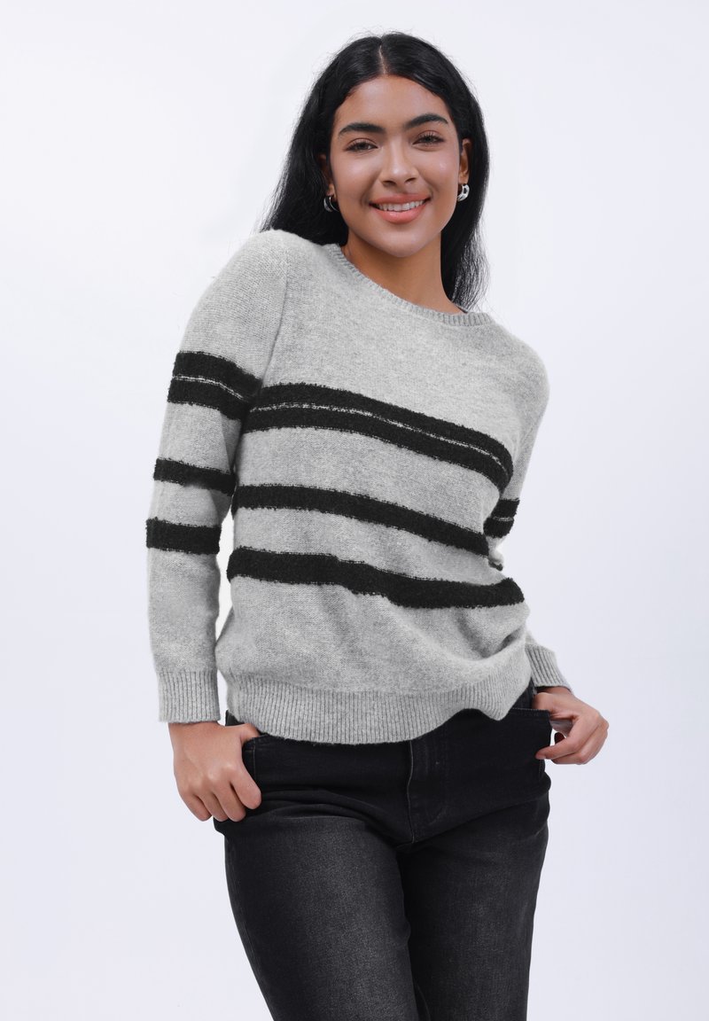 Hellgrauer Pullover mit schwarzen horizontalen Streifen, Rundhalsausschnitt und gerippten Bündchen. Kombiniert mit schwarzen Jeans im lässigen Schnitt.