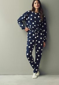 Tumedate polka dot vabaaja komplekt, mis sisaldab ümmarguse kaela aukuga sweatshirti ja elastse vöökoha ning valgete punktidega pükse; pehme kangas ja mansettidega varrukad.
