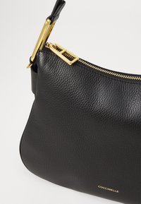 Borsa a spalla in pelle nera con texture a granuli, zip dorata e dettagli metallici. Presenta un logo del marchio discreto.