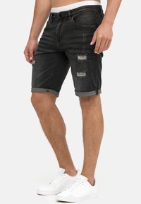 Zwarte denim shorts met een versleten ontwerp, met rafelige randen en gescheurde details. Omgeslagen zoom en een slanke pasvorm. Gecombineerd met witte sneakers.