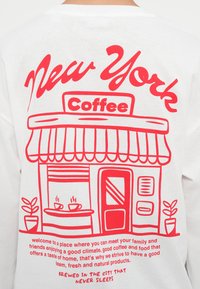 Άσπρο T-shirt με κόκκινο γραφικό σχέδιο καφέ με την επιγραφή «New York Coffee», που απεικονίζει λεπτομέρειες όπως φλιτζάνια, πόρτα και φυτό.