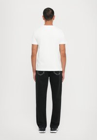 Hvit bomull t-skjorte sammen med svarte jeans. Jeansene har baklommer med dekorativ søm. Modellen har på seg svart-hvite sneakers.