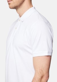 Biała bawełniana koszulka polo z kołnierzykiem, krótkimi rękawami i zapięciem na trzy guziki. Gładka faktura i minimalistyczny design.