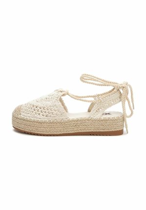 Espadrille tejido en color beige, con suela de yute, tiras entrelazadas y parte superior texturizada. El diseño incluye un cierre atado en el tobillo.