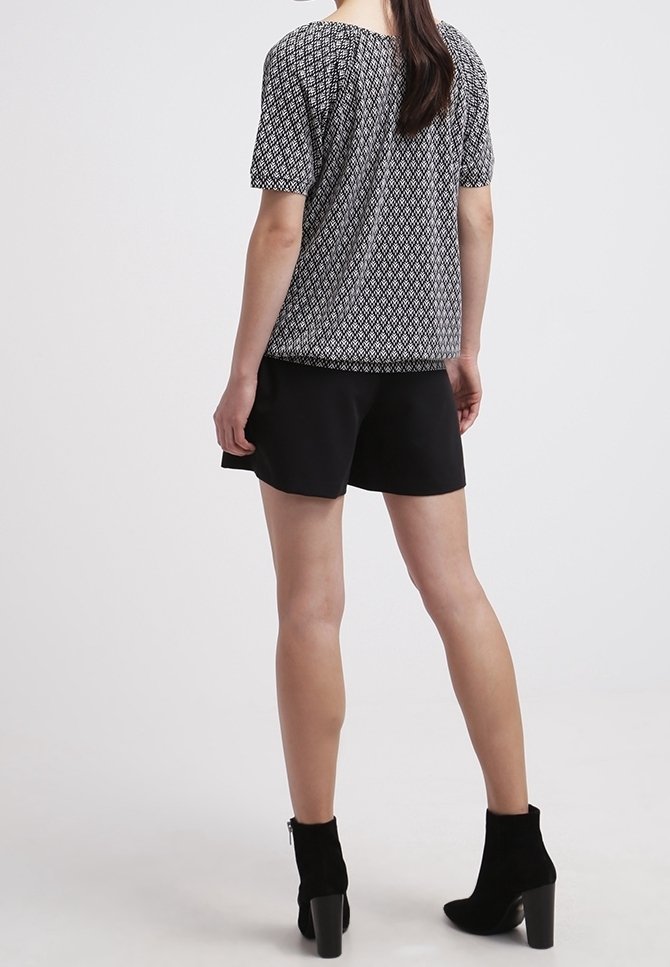 Svartvitt mönstrad kortärmad topp med en avslappnad passform, kombinerad med svarta shorts och ankelboots med klumpig klack.