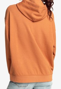 Felpa arancione oversize con cappuccio regolabile, polsini e orlo a costine. Realizzata in materiale morbido con una texture liscia e senza motivi visibili.