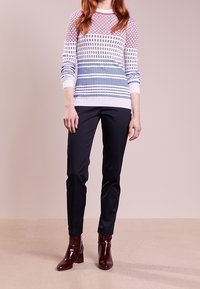 Färgglad stickad tröja med geometriska mönster, lätt tyg, kombinerad med figurnära svarta byxor och blanka burgundy ankelskuggar.