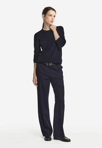 Granatowy sweter dzianinowy z długimi rękawami, w połączeniu z szerokimi spodniami w tym samym odcieniu. Oba elementy mają gładką fakturę i luźny krój.