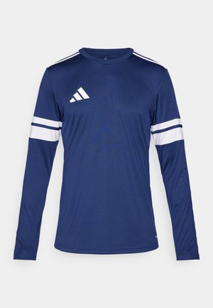 Majica z dolgimi rokavi v temno modri tkanini. Ima bele črte na rokavih in tri bele črte na rami. Logo Adidas na prsih.