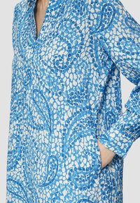 Blaue gemusterte Hemdkleid mit langen Ärmeln, die verschiedene blaue und weiße abstrakte Designs aufweist, einen Kragen und Seitentaschen. Textil mit Struktur.
