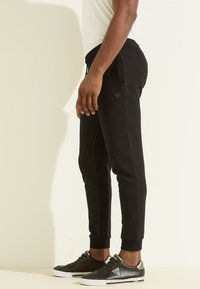 Zwarte tapered joggers met zijzakken, gemaakt van zachte stof. Bevat een driehoekig logo accent en een geribbelde manchette bij de enkel.