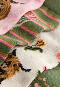 Verschiedene Strickstoffe mit einer Vielzahl von Mustern: grüne Streifen mit Pink, florale Designs und ein braunes Tiermotiv.