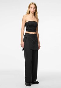Top nero senza spalline con design aderente e texture liscia, abbinato a pantaloni neri a vita alta e gamba larga, con un dettaglio di fascia annodata.