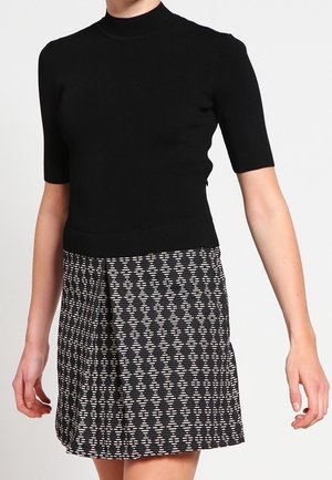 Vrouw draagt een zwart coltrui met korte mouwen en een zwart-witte knie-lange rok met patroon.