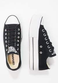 Sneakers neri in tela con suole in gomma bianca, punta tonda e design classico con lacci. Presentano una patch con il logo sulla linguetta e dettagli laterali.