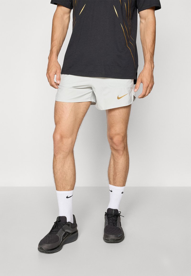 Light gray Nike shorts with a small gold logo, paired with black athletic shoes and white socks. Black T-shirt with a graphic design.