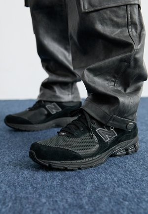 Black New Balance sneakers feature a mix of mesh and suede materials, a textured black outsole, and a prominent logo on the side.