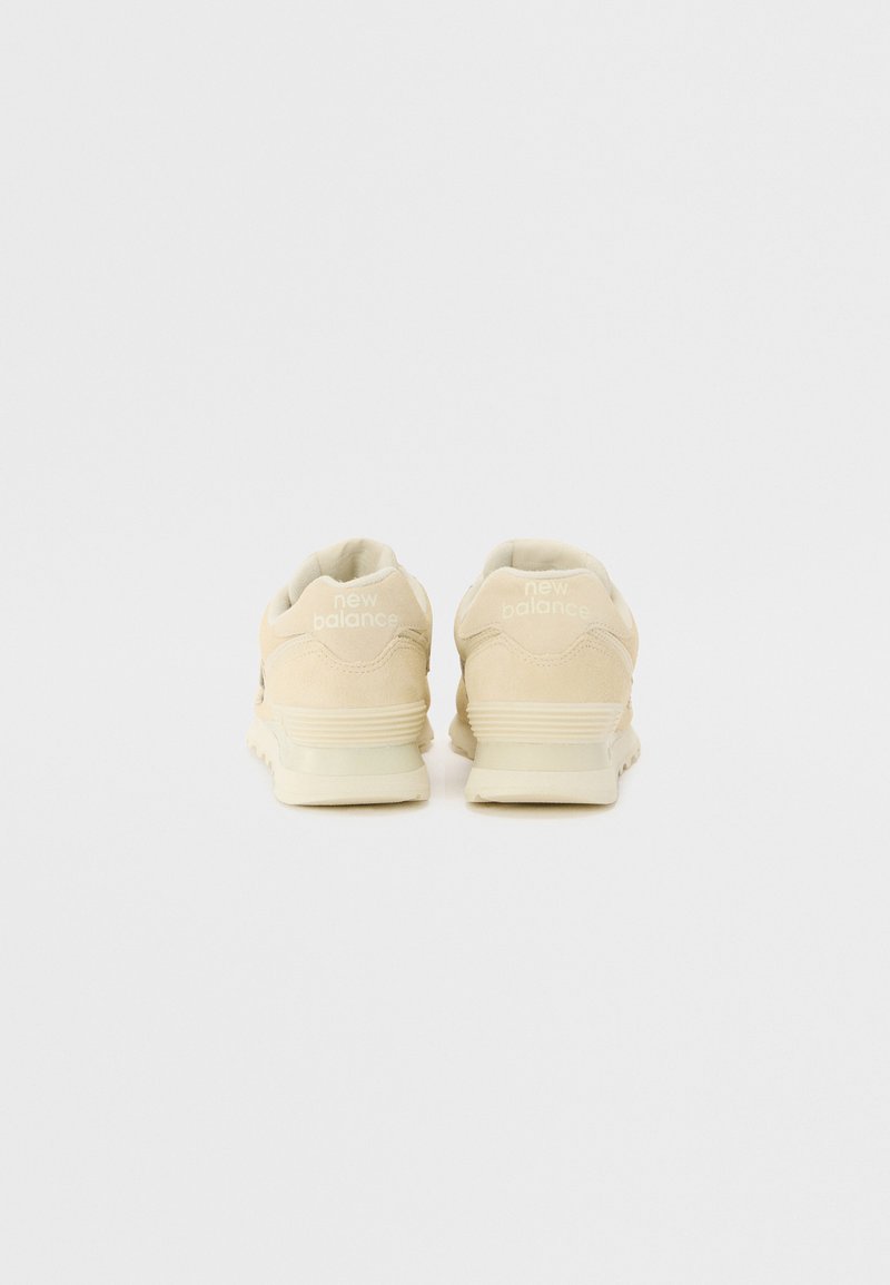Zapatillas de ante beige con una lengüeta texturizada en el talón, suela de goma y logo de "new balance" en blanco en la parte trasera. Diseño clásico de cordones.
