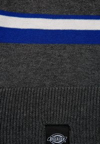 Dunkelgrauer Strickstoff mit weißen und blauen horizontalen Streifen und einem kleinen schwarzen rechteckigen Dickies-Label.