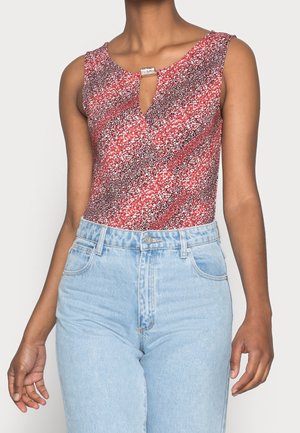 Czerwony body w wzór z dekoltem w serek i detalem w postaci klucza, z metalicznym akcentem. Połączone z jasnoniebieskimi dżinsami z wysokim stanem.