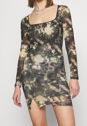 Woman wearing a long-sleeve, square-neck tie-dye dress with a small front slit and layered silver necklaces.