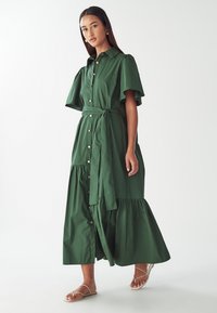 Zelené dlouhé šaty s krátkými nařasenými rukávy, zapínáním na knoflíky vpředu a zavinovacím lemem. Součástí je sladěný pásek pro zvýraznění pasu.