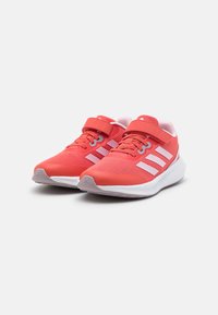 Zapatillas deportivas rojas con parte superior de malla, cordones elásticos y correa de gancho y bucle. Suela blanca y tres rayas blancas en el lateral.