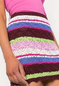 Falda de punto colorida con rayas horizontales en burdeos, verde, rosa, azul y blanco, con un dobladillo con forma de concha y un intrincado patrón de encaje.