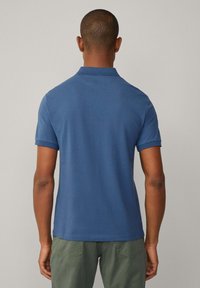 Námořnická modrá polo tričko s krátkým rukávem. Obsahuje klasický límec a jednobarevnou látku. Kombinováno s olivově zelenými kalhotami.